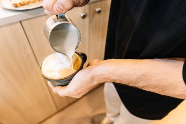 Barista elinde fincanla, latte sanatı için buğulanmış süt dolduruyor.