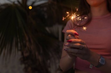 Bir kadın elinde maytap tutuyor. Görüntünün sıcak ve şenlikli bir havası, kutlamaları ve özel etkinlikleri var..