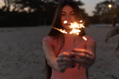 Kırmızı kazaklı genç kadın plajda yanan bir mum tutuyor. Tatil ve rahatlama kavramı.