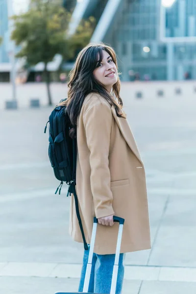 Genç bir kadın iş seyahatinde, bavulunu çekiyor ve sırt çantası taşıyor.