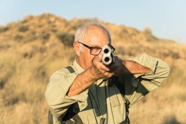Kıdemli avcı çift namlulu av tüfeğini hedef alıyor, av sırasında açık havaya odaklanıyor.