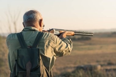 Kırsalda avlanan kıdemli bir adam günbatımına nişan alıyor, dışarıda hobi ediniyor.