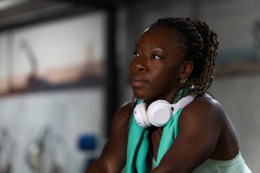 Boyun ve havlularda kulaklıkları olan yorgun sporcu kadın fitness kulübünde yoğun idmandan sonra mola veriyor.