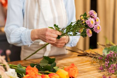 Çiçekçi çiçek buketi için pembe kasımpatı hazırlıyor. Çiçekçinin ahşap masasında renkli çiçeklerle çevrili.