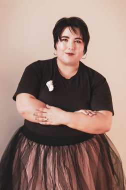 Siyah tişörtlü, kısa saçlı ve göğsünde çapraz kolları olan şişman bir esmerin portresi.