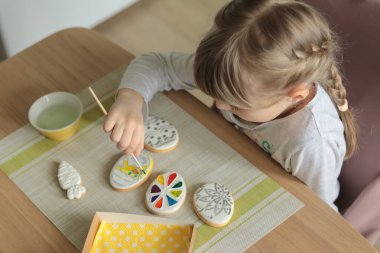 At kuyruklu kız, masada otururken fırçayla fırçalı kurabiyeler boyuyor.