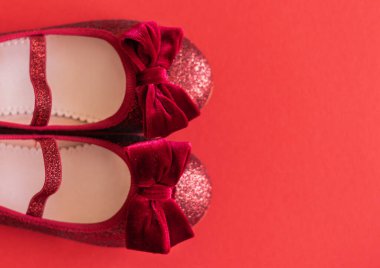 Kırmızı arka planda kadife fiyonklu parlak kırmızı balerinler.