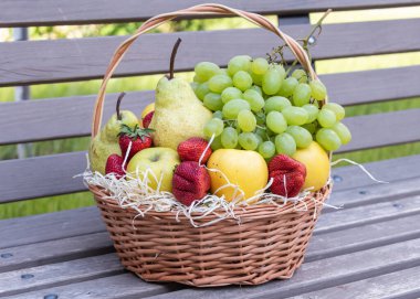 Taze meyve ve böğürtlen dolu yuvarlak sepet ahşap bir bankta duruyor.