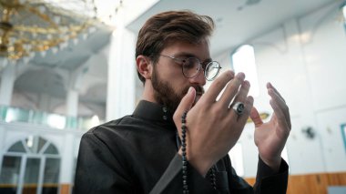 Müslüman erkek dua ediyor ve camide tespihle dua ediyor. Mescid-i Haram 'da namaz kılan genç Müslüman adam. İslam 'a tapınma ve şeyhle bağlılık kavramı..