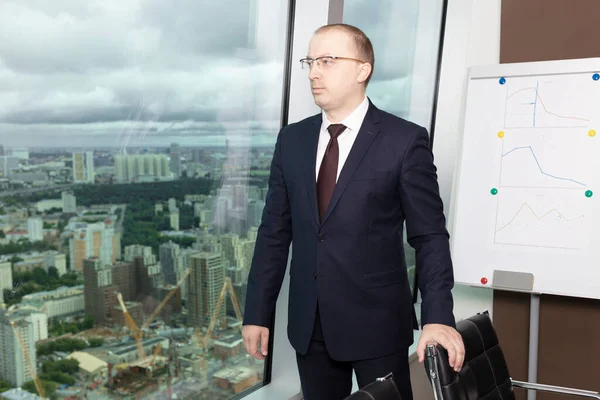 İş kıyafetleri yöneticisi toplantıdan sonra dikkatle ofis penceresinden dışarı bakar ve iş müsabakasına karar vermek için plan yapar, kapatır.