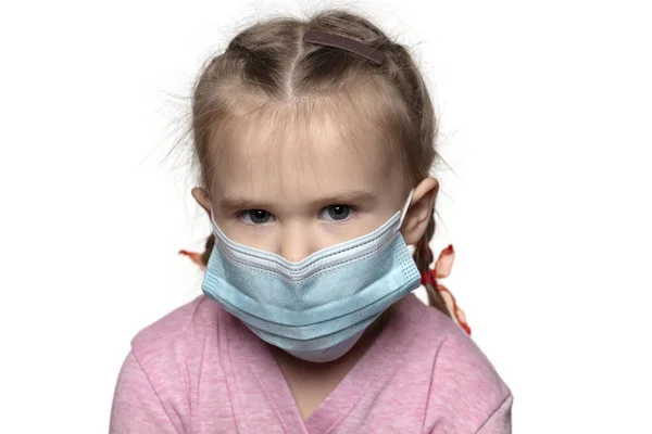 Saçları örgülü ve mavi tıbbi maske takan güzel Avrupalı kız kameraya bakıyor. Başını beyaz arka plana eğiyor, yakın plan.