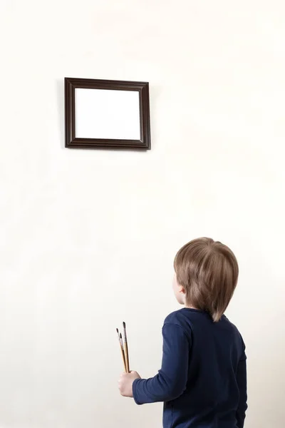 Beyaz fırçaları kalın saçlı yakışıklı beyaz tenli çocuk duvardaki yatay çerçevenin önünde duruyor ve ona bakıyor, kapanıyor.