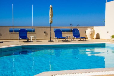 Akdeniz kıyısındaki bir otelde güneş yatakları ve havuz kenarında bir şemsiye.