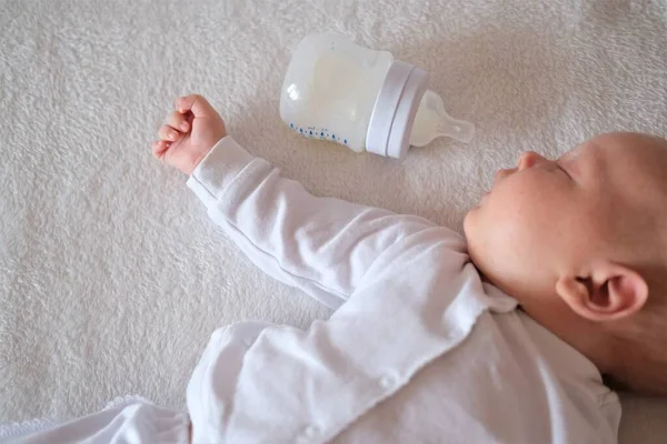 De pasgeboren baby heeft moedermelk uit een fles gegeten. jongen of meisje slapen op bed op witte achtergrond Stockafbeelding