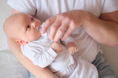 Bir baba yeni doğmuş bebeğini kucağına alıp besler. Bebeğin yüzünde ve kafasında irin var..