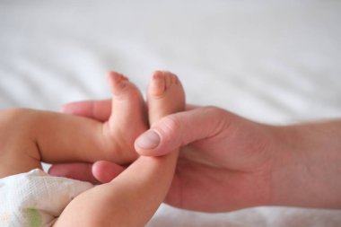 Baba, yeni doğmuş bir bebeğin ayaklarını kollarında tutuyor. Eller ve ayaklar beyaz arka planda yakın plan.
