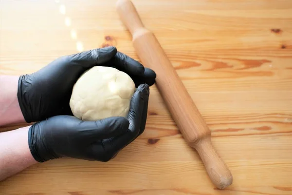 Mains masculines en gants noirs sur le fond d'une table en bois.Pâte à pain, khinkali, boulettes et pâtisseries. Concept de cuisine. — Photo