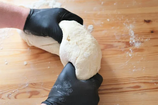 Chef en guantes negros amasa la masa para hacer pan, khinkali, albóndigas y pasteles. Manos masculinas sobre un fondo de mesa de madera. Concepto de cocina. —  Fotos de Stock