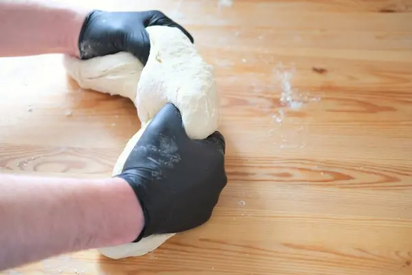 Chef en gants noirs pétrit pâte pour faire du pain, khinkali, boulettes et pâtisseries. Mains masculines sur un fond de table en bois. Concept de cuisson. — Photo