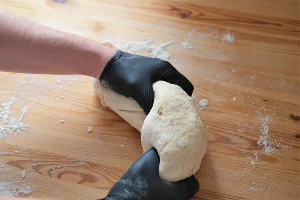 Chef en gants noirs pétrit pâte pour faire du pain, khinkali, boulettes et pâtisseries. Mains masculines sur un fond de table en bois. Concept de cuisson. — Photo