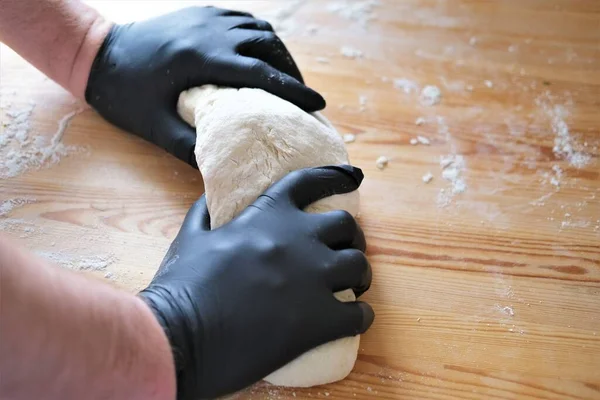 Chef en gants noirs pétrit pâte pour faire du pain, khinkali, boulettes et pâtisseries. Mains masculines sur un fond de table en bois. Concept de cuisson. — Photo