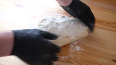 Siyah eldivenli şef ekmek, khinkali, hamur işi ve hamur işi yapmak için hamur yoğurur. Erkek elleri, tahta bir masa arkasına yaslanmış. Yemek pişirme konsepti.