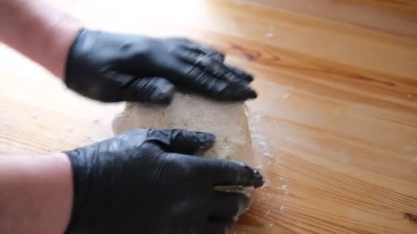 Kuchař v černých rukavicích hnětá těsto na chleba, khinkali, knedlíky a pečivo. Mužské ruce na pozadí dřevěného stolu. Koncept vaření. — Stock video