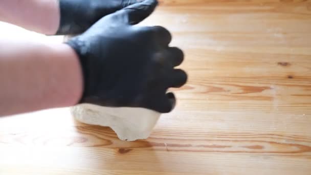 Σεφ σε μαύρα γάντια ζυμώνει ζύμη για την παρασκευή ψωμιού, khinkali, ζυμαρικά και αρτοσκευάσματα. Αρσενικά χέρια πάνω σε ξύλινο τραπέζι φόντο. Έννοια μαγειρικής. — Αρχείο Βίντεο