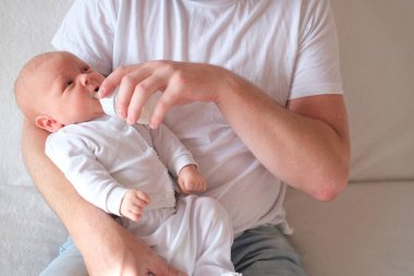 Bir baba yeni doğmuş bebeğini kucağına alıp besler. Bebeğin yüzünde ve kafasında irin var.