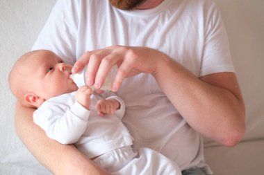 Bir baba yeni doğmuş bebeğini kucağına alıp besler. Bebeğin yüzünde ve kafasında irin var.