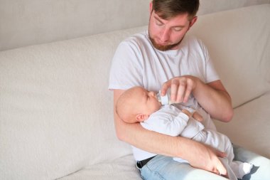 Bir baba yeni doğmuş bebeğini kucağına alıp besler. Bebeğin yüzünde ve kafasında irin var.