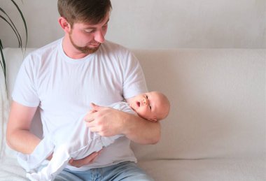 Bir baba üç aylık oğlunu kollarına alır.