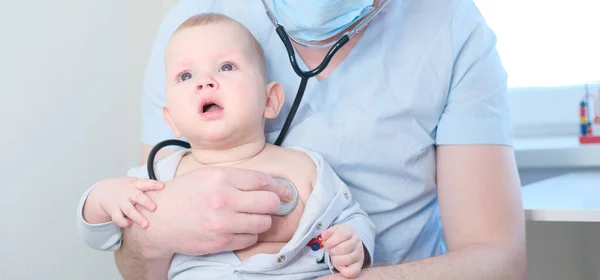 Çocuk doktoru kucağında küçük bir çocuk tutuyor. Çocuk doktoru steteskoplu çocuğu dinler.