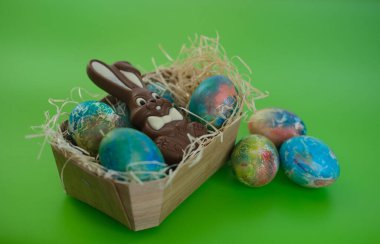 Çikolatalı Paskalya tavşanı yeşil arka planda renkli yumurtalarla dolu bir sepette yatıyor.
