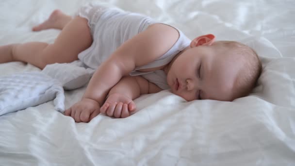 Un bambino che allatta dorme in un letto su lenzuola bianche. — Video Stock