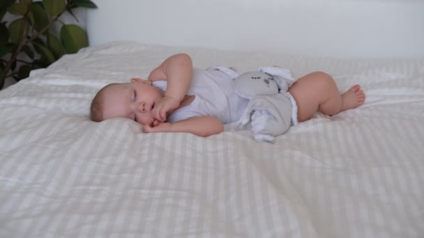Un bebé lactante duerme en una cama sobre sábanas blancas. — Vídeo de stock