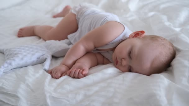 Een verzorgende baby slaapt in een bed op wit beddengoed. — Stockvideo