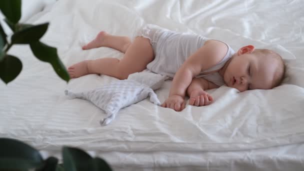 Un bebé lactante duerme en una cama sobre sábanas blancas. — Vídeo de stock