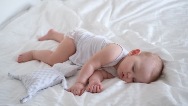 Un bambino che allatta dorme in un letto su lenzuola bianche. — Video Stock