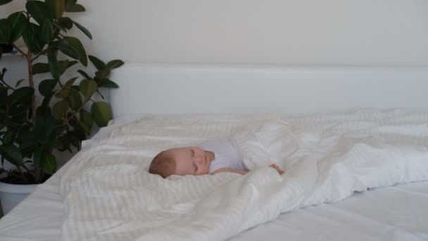 Een verzorgende baby slaapt in een bed op wit beddengoed. — Stockvideo