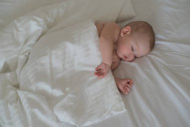 Küçük bir çocuk beyaz bir yatakta uyur. Beyaz arka planda uyuyan küçük bir çocuğun portresi.