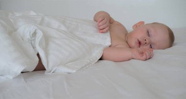 Küçük bir çocuk beyaz bir yatakta uyur. Beyaz arka planda uyuyan küçük bir çocuğun portresi.