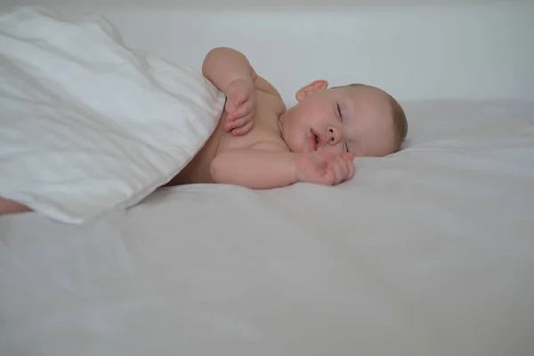 一个小孩睡在白色被褥上的床上 白色背景上睡着的小男孩的画像 — 图库照片