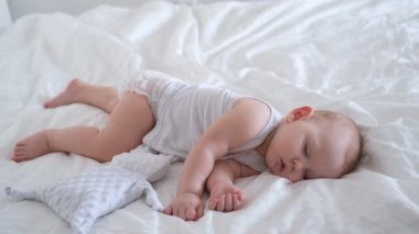 Hemşirelik yapan bir bebek beyaz çarşafların üzerinde bir yatakta uyur..