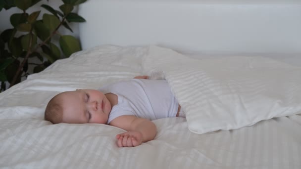 Een verzorgende baby slaapt in een bed op wit beddengoed. — Stockvideo