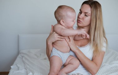 Genç bir anne bebeğini kollarında tutuyor, bebek ağlıyor, dişleri dökülüyor ya da midesi ağrıyor.