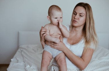 Genç bir anne bebeğini kollarında tutuyor, bebek ağlıyor, dişleri dökülüyor ya da midesi ağrıyor.