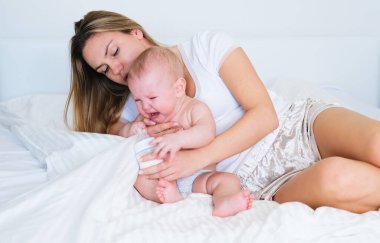 Genç bir anne bebeğini kollarında tutuyor, bebek ağlıyor, dişleri dökülüyor, uyumak istiyor ya da karnı ağrıyor.