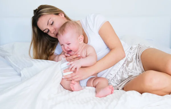 Genç bir anne bebeğini kollarında tutuyor, bebek ağlıyor, dişleri dökülüyor, uyumak istiyor ya da karnı ağrıyor.