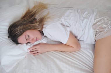 Genç, güzel bir kız beyaz bir yatakta uyuyor. Kadın portresi.